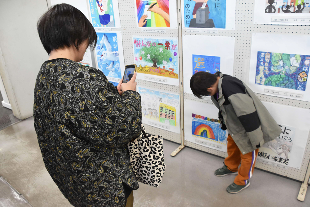 ポスター展会場で自分の書いた絵と一緒に写真を撮っている親子